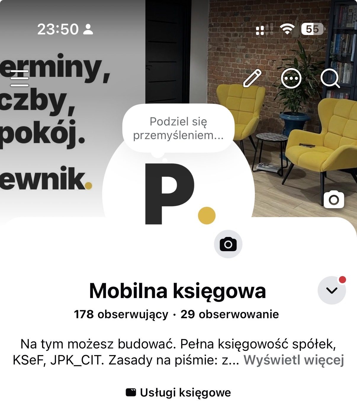 Biurko w biurze Pewnik: monitor, klawiatura, okulary i kwiaty, w tle ceglana ściana
