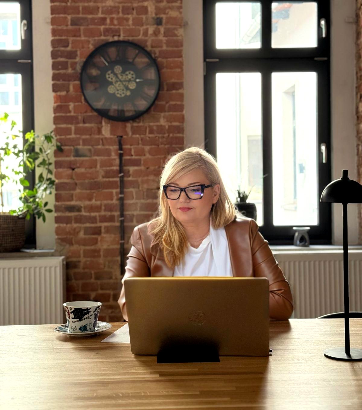 Praca przy laptopie w biurze Pewnik: ceglana ściana, duże okna, zegar